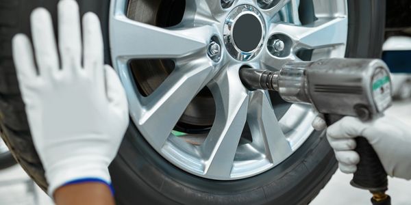 Mechanic using a power tool to tighten a car wheel lug nut.