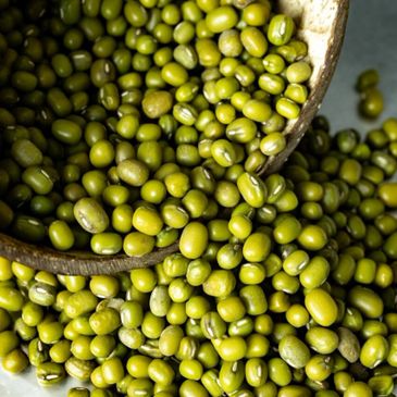 Close-up of green mung beans spilling from a wooden container.