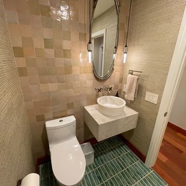 Modern bathroom with green tiled floor and oval mirror above a floating sink.