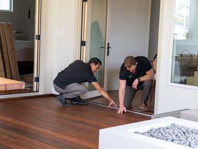 Two men inspecting a wooden floor near a glass door inside a modern home.