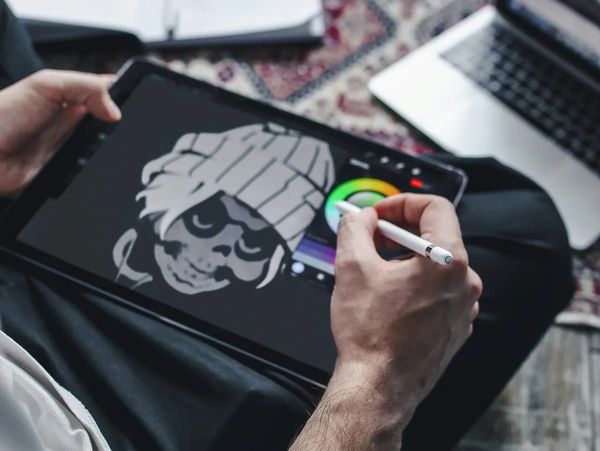 Person digitally drawing a skull with a beanie on a tablet using a stylus.