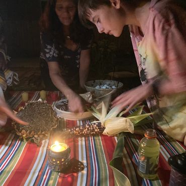 Two people examine items on a striped tablecloth illuminated by candlelight at night.