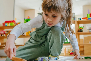 Young girl sweeping floor with brush and dustpan indoors.