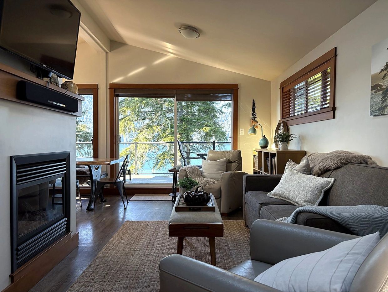 Cozy living room with a fireplace and large window showing trees and a lake.