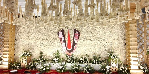 Elaborate floral wedding backdrop with divine imagery and hanging flower garlands.