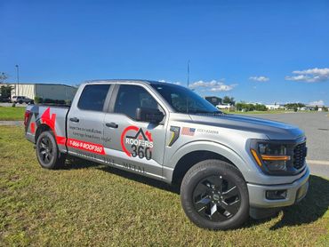 Silver pickup truck with Roofers 360 branding and contact details parked on grass.