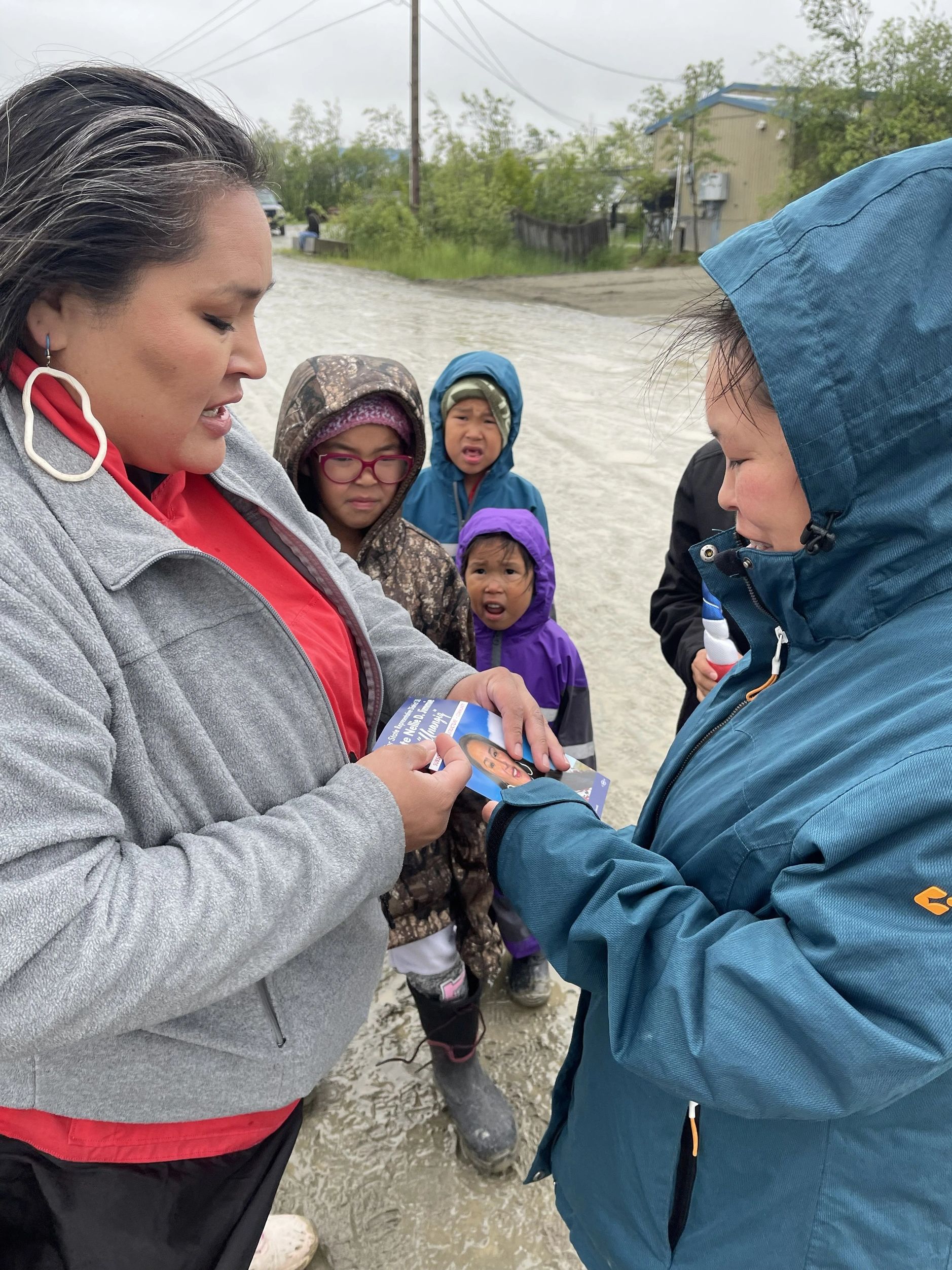 Two women showing a photo to children outdoors on a rainy day.