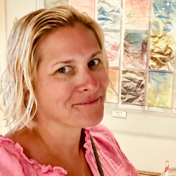 Woman with blonde hair wearing a pink top, smiling.
