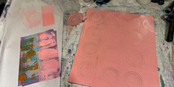 Pink sheet with circular patterns next to a painted abstract art piece.