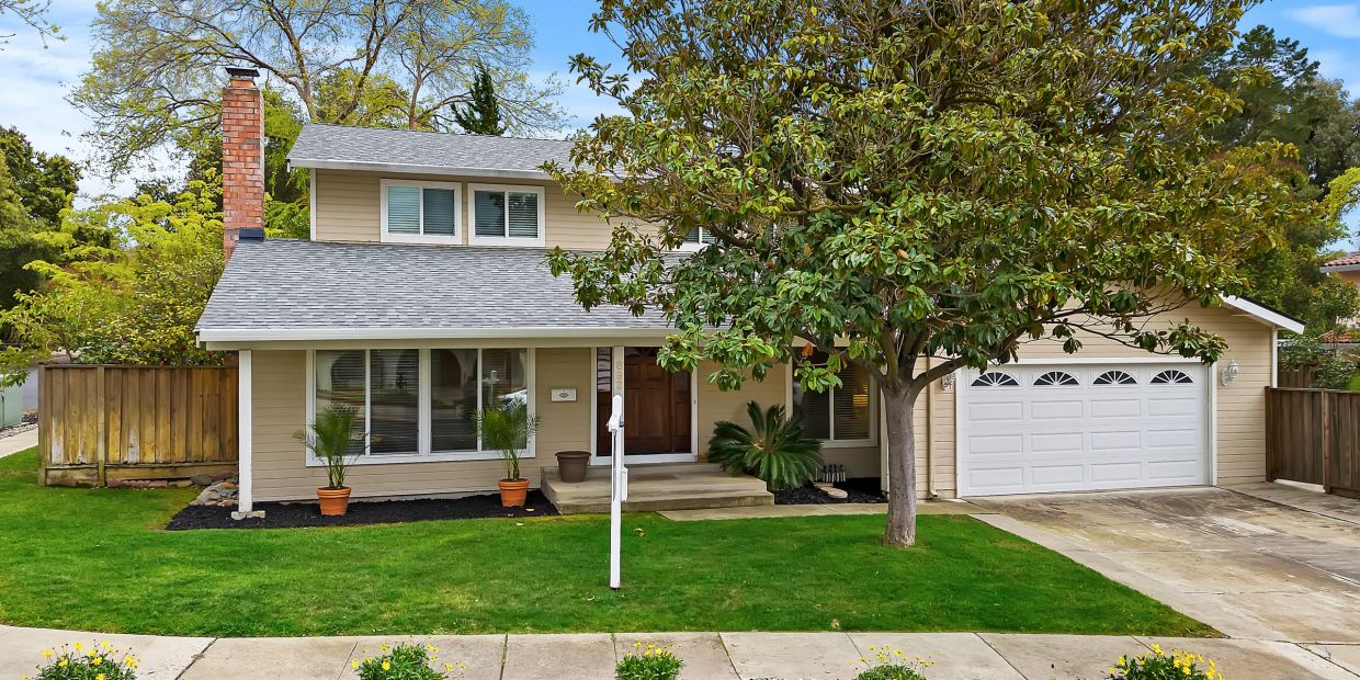 A cozy suburban house with a green lawn and large tree in front.