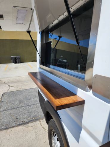 Close-up of a food truck serving window with a wooden counter and support arms.