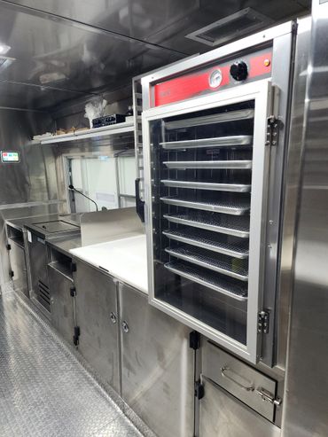 Interior of a stainless steel commercial kitchen with oven and prep area.