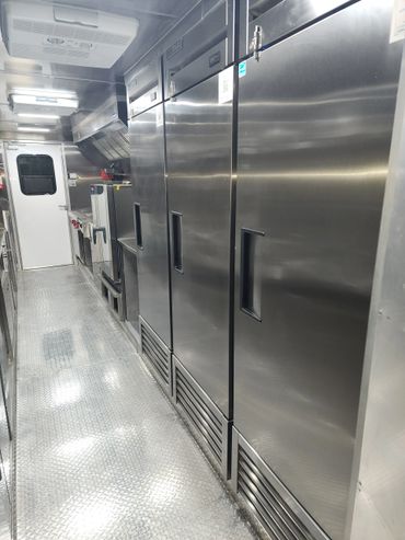 Interior of a clean, stainless steel commercial kitchen with refrigerators and cooking appliances.