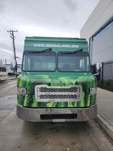 Front view of a green food truck with leafy vegetable design and website URL.