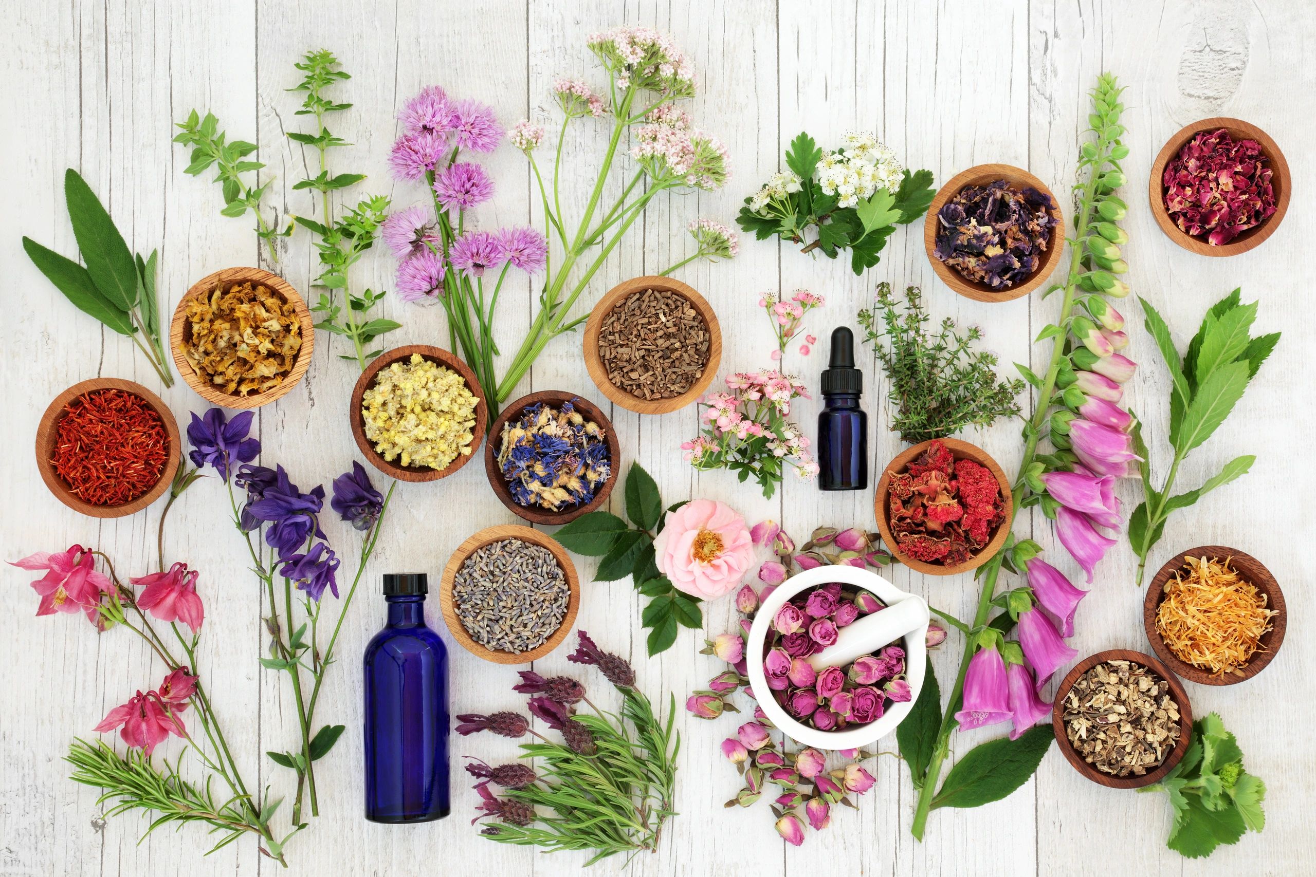 Various dried herbs, flowers, and essential oil bottles on a wooden surface.