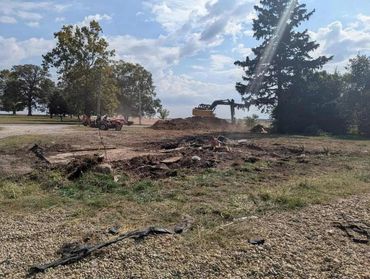 Excavator digging soil with workers and tractor nearby on a sunny day.