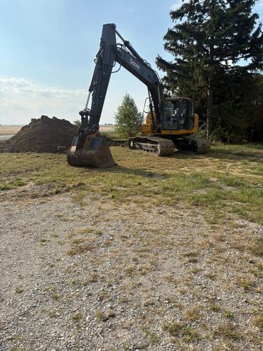 A Deere excavator parked on grassy land near a pile of dirt.