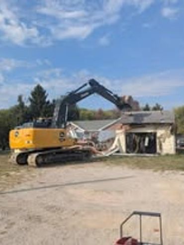 Excavator demolishing a small building under a partly cloudy sky.