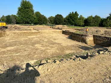 Construction site with large excavated area and worker in orange vest.