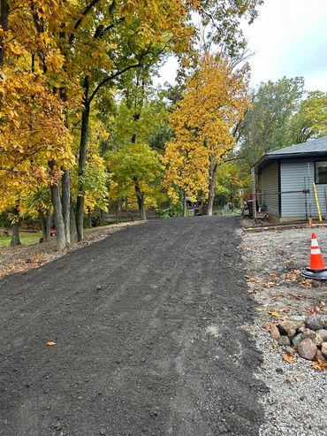 Freshly laid gravel driveway surrounded by autumn trees near a house.