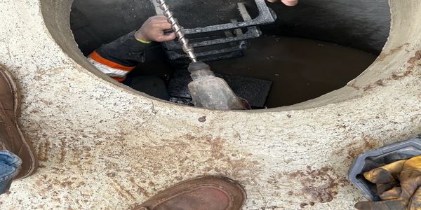 Worker drilling inside a concrete manhole with tools around.