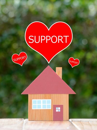 Small paper house with a paper heart saying "Support" above with blurry background