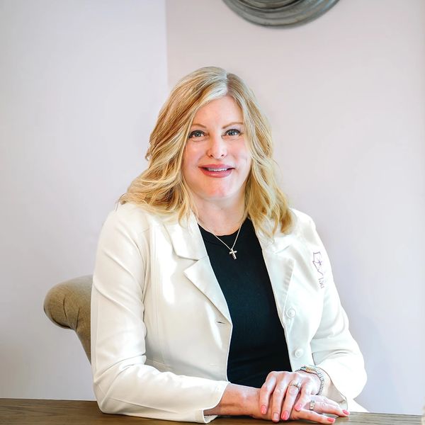 Smiling woman in a white coat sitting at a desk.