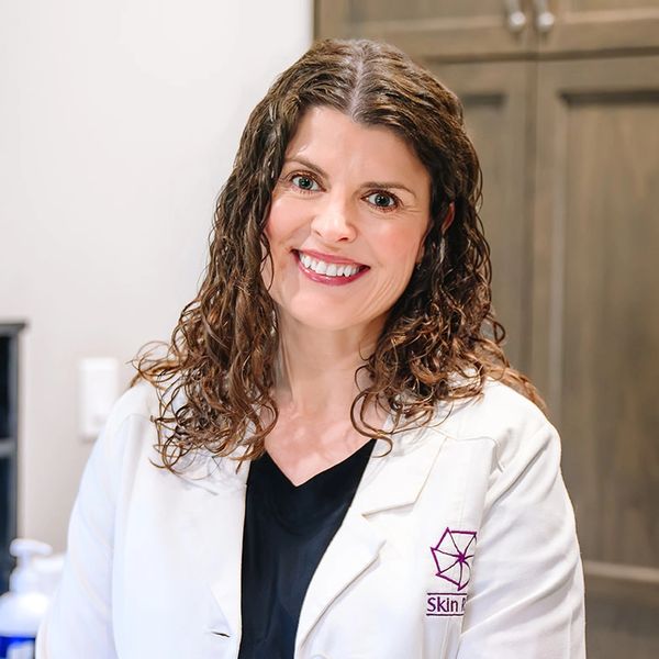 Smiling woman in a white lab coat indoors.