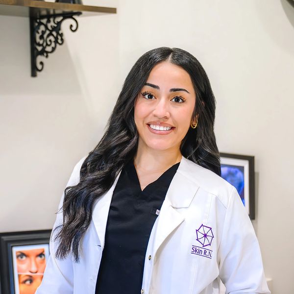 Smiling woman in a white lab coat with Skin R.N. logo.