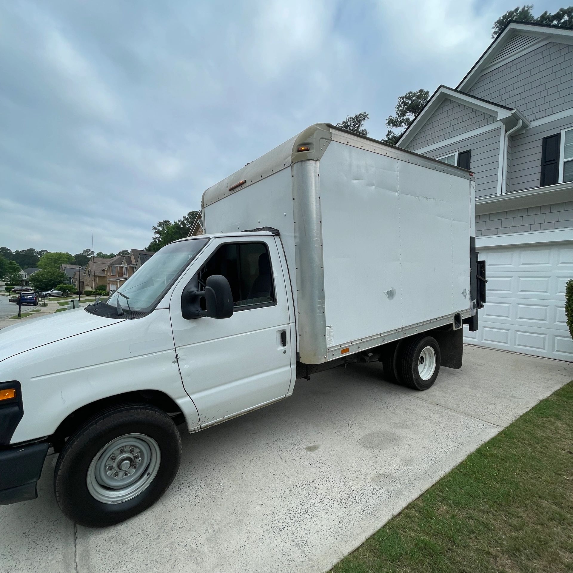 White box truck parked on a driveway beside a house.