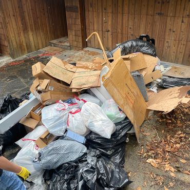 Pile of garbage bags and cardboard boxes outside a wooden building.