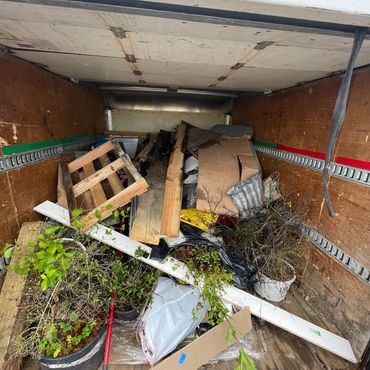 Truck bed filled with wooden planks, plants, and assorted debris.