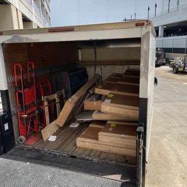 Open truck loaded with wooden crates and red hand trucks outside a department store.