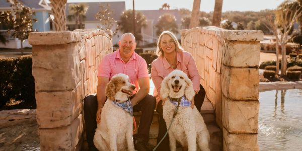 Couple with two white poodles on a stone bridge.