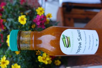 Bottle of Peppa Sauce with flowers in background.