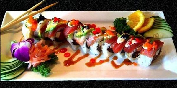 Colorful sushi roll with garnishes and dipping sauce.