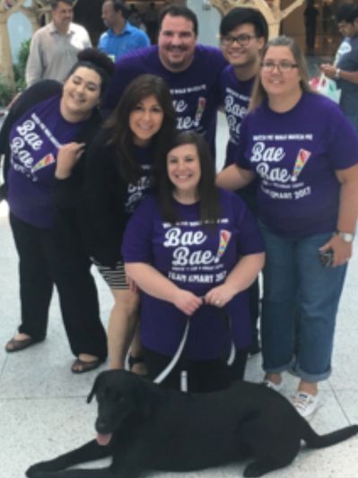 group of people wearing purple t shirts one holding leash of black lab