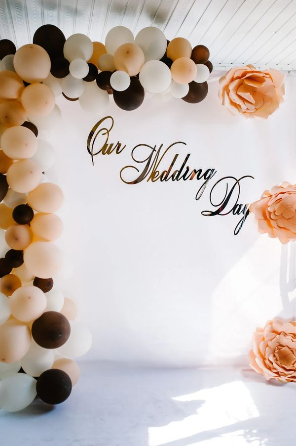 Elegant wedding backdrop with balloons and large peach flowers.