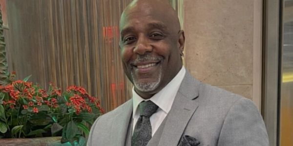 A smiling man in a gray suit posing indoors near plants.