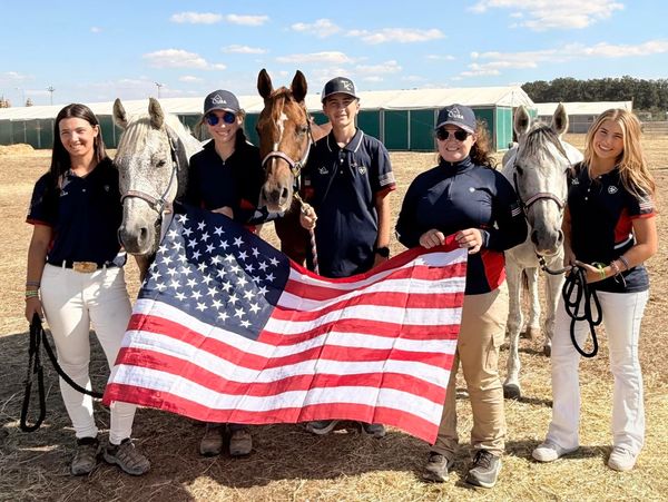 Five equestrians with horses holding an American flag outdoors.