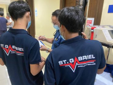 Two St. Gabriel Ambulance Service workers consulting a medical professional in a hospital.