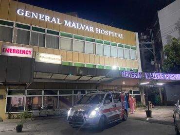 Night view of General Malvar Hospital with ambulance and emergency signs.
