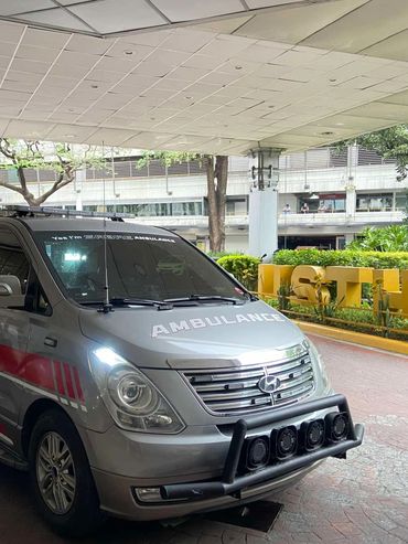 Silver ambulance vehicle parked under a covered area near a hospital.