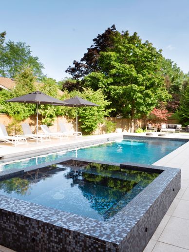 Image of backyard pool and a tiled hot tub in the foreground.