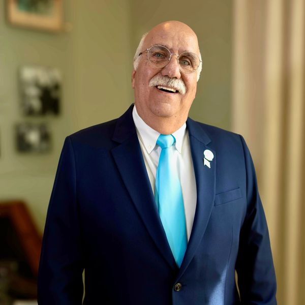 Older man smiling in a navy suit and blue tie.