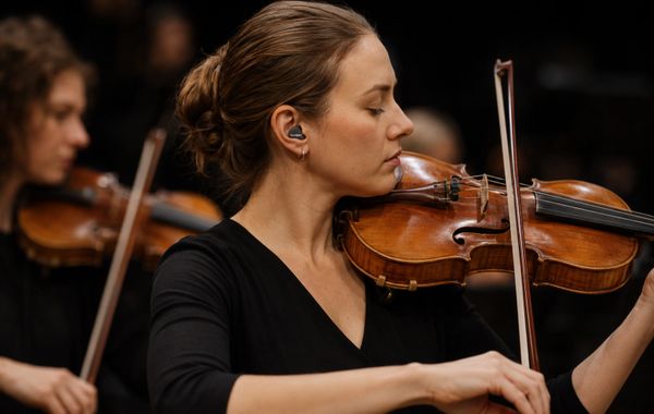 Voilinist in concert concentrating with her eyes closed in black top wearing musicians hearing prote