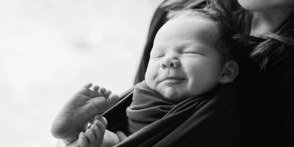 Black and white photo of a smiling newborn baby wrapped in a blanket.