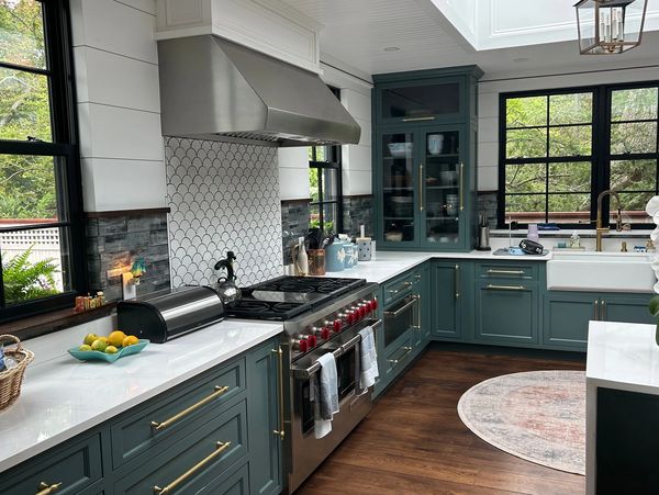 Modern kitchen with teal cabinets, white countertops, and large windows overlooking greenery.