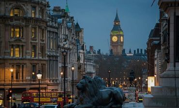 Evening view of London's Big Ben with street lights and lion statue in foreground.