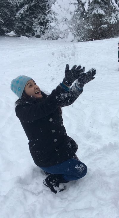Woman joyfully playing with snow in a snowy forest landscape.